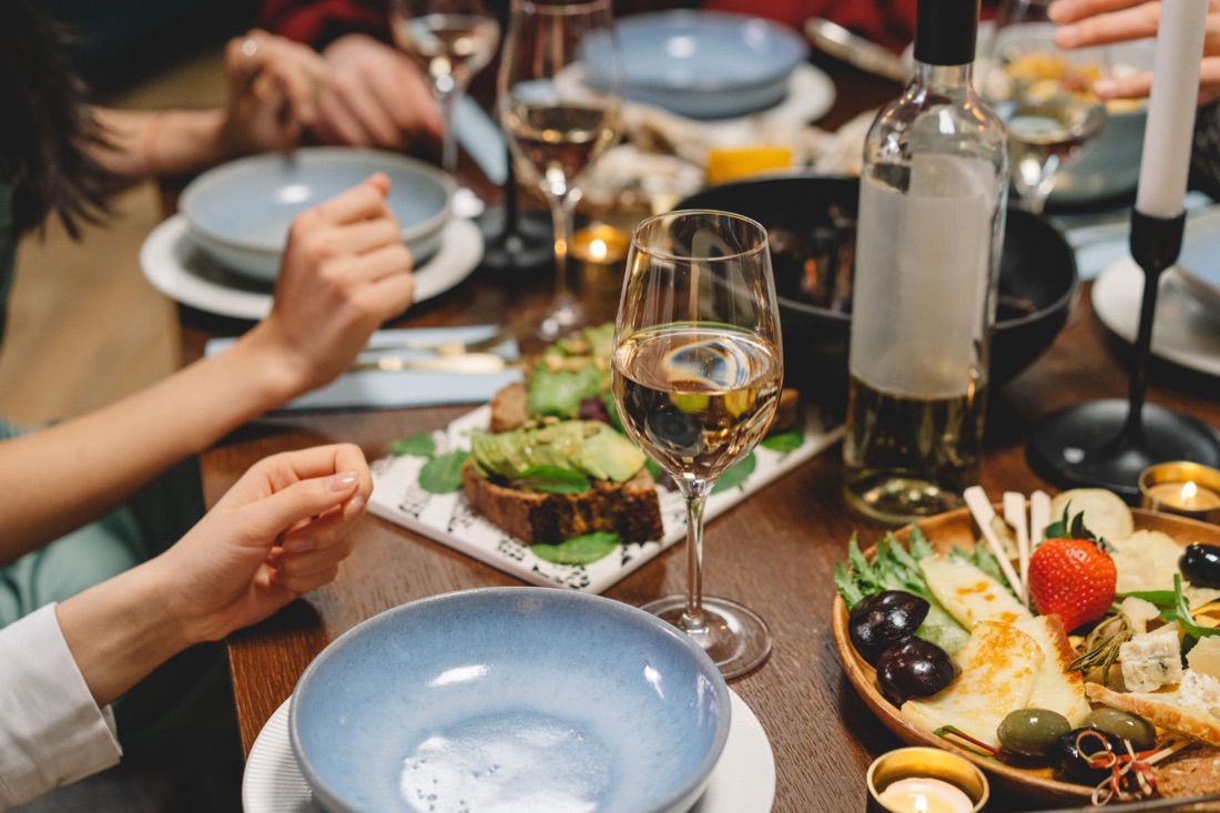 A candlelit dinner table with white wine, blue bowls and a cheese board.
